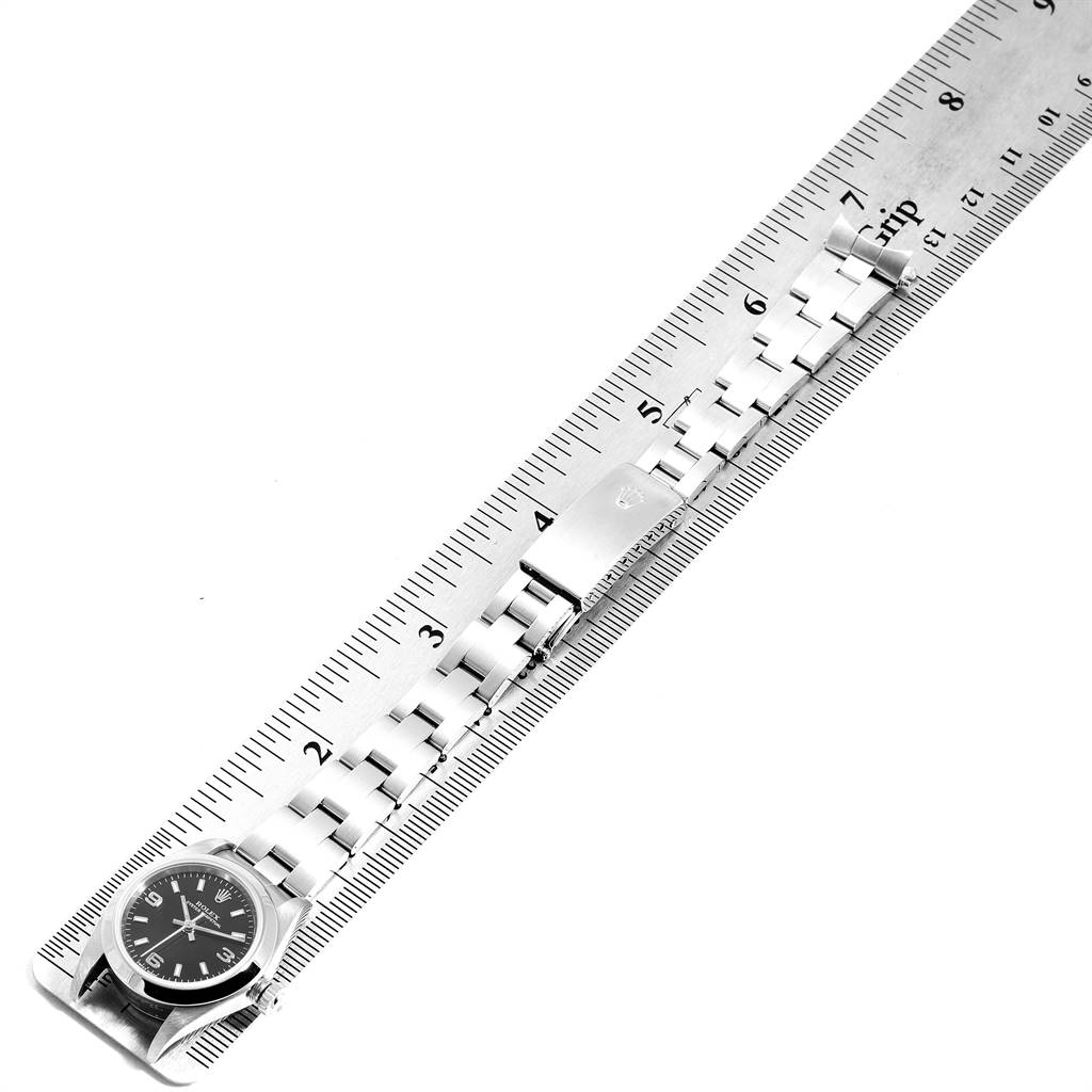 This image displays a Rolex Oyster Perpetual 76080 Women's Stainless Steel Black Dial 76080 Women's Stainless Steel Black Dial watch laid flat with its entire metal bracelet aligned next to a ruler.