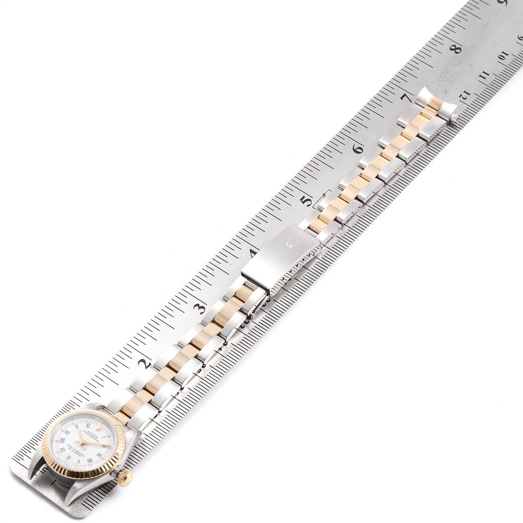 The image shows a Rolex Oyster Perpetual 67193 Women
s Steel and Gold (two tone) White Dial 67193 Women
s Steel and Gold (two tone) White Dial watch positioned alongside a ruler, highlighting its face, bracelet, and clasp.