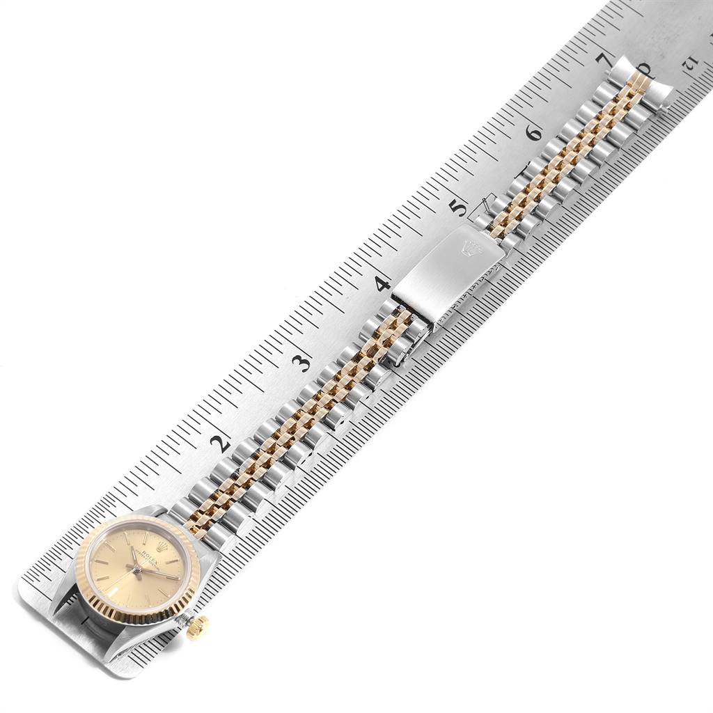 The image shows a top view of a Rolex Oyster Perpetual 67193 Women
s Steel and Gold (two tone) Champagne Dial 67193 Women
s Steel and Gold (two tone) Champagne Dial watch, including its dial, bezel, and metallic bracelet aligned with a ruler.