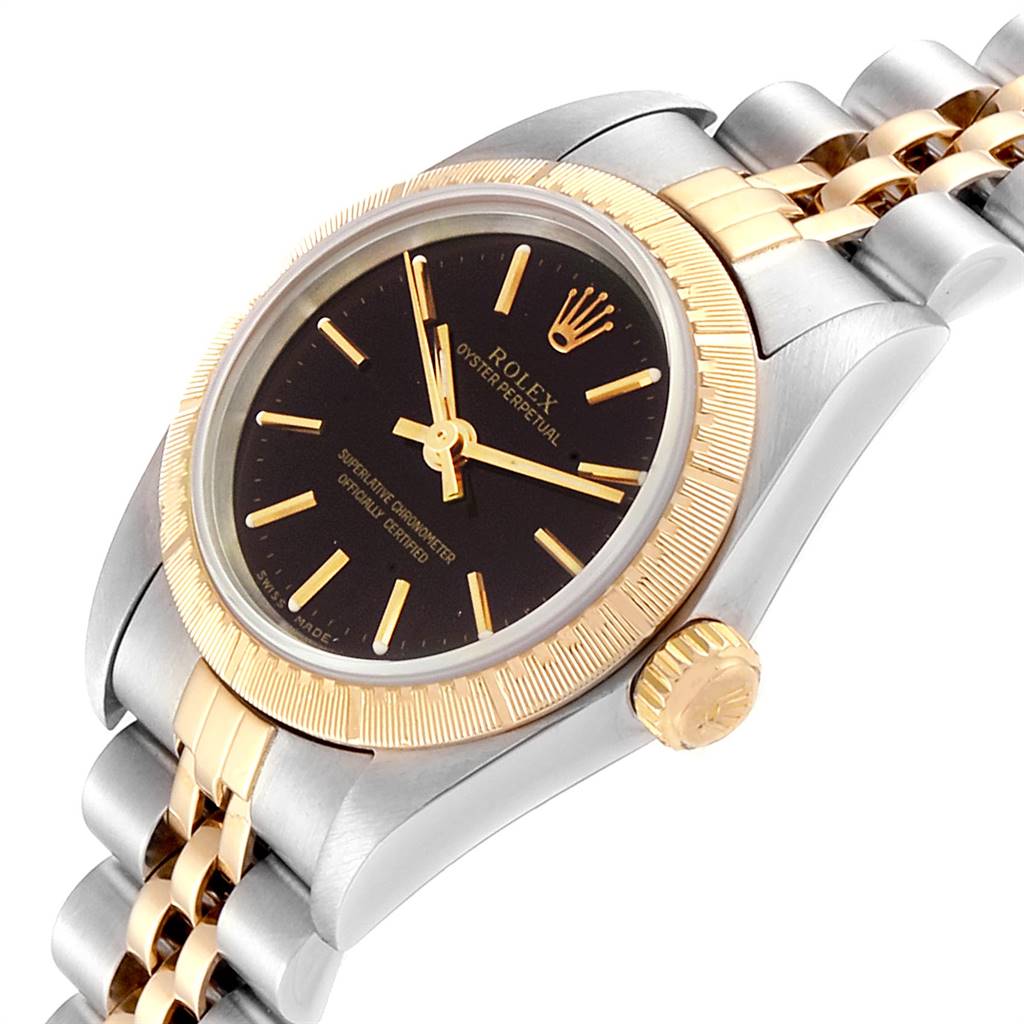 The image showcases a Rolex Oyster Perpetual 76243 Women
s Steel and Gold (two tone) Black Dial 76243 Women
s Steel and Gold (two tone) Black Dial watch angled to display its dial, bezel, crown, and part of its metal bracelet.