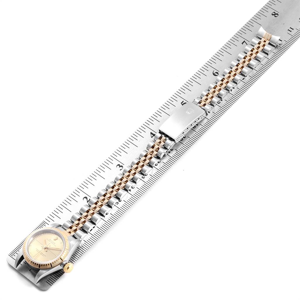 The Oyster Perpetual Rolex watch is shown from a top-down angle, displaying the face, bracelet, and clasp laid on a ruler.