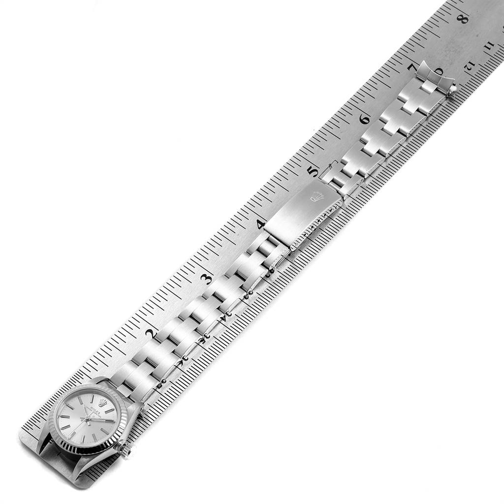 The image shows the Rolex Oyster Perpetual 67194 Women's Stainless Steel Silver Dial 67194 Women's Stainless Steel Silver Dial watch and its metal bracelet laid against a ruler, viewed from above.