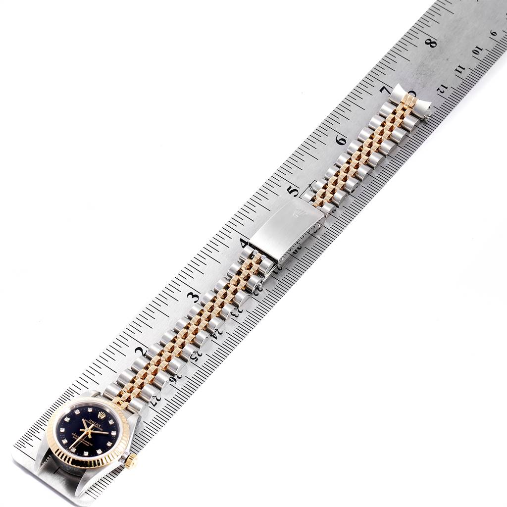 The image shows a top-down view of a Rolex Oyster Perpetual 76193 Women's Steel and Gold (two tone) Black Dial 76193 Women's Steel and Gold (two tone) Black Dial watch, focusing on its face and bracelet, aligned with a ruler.