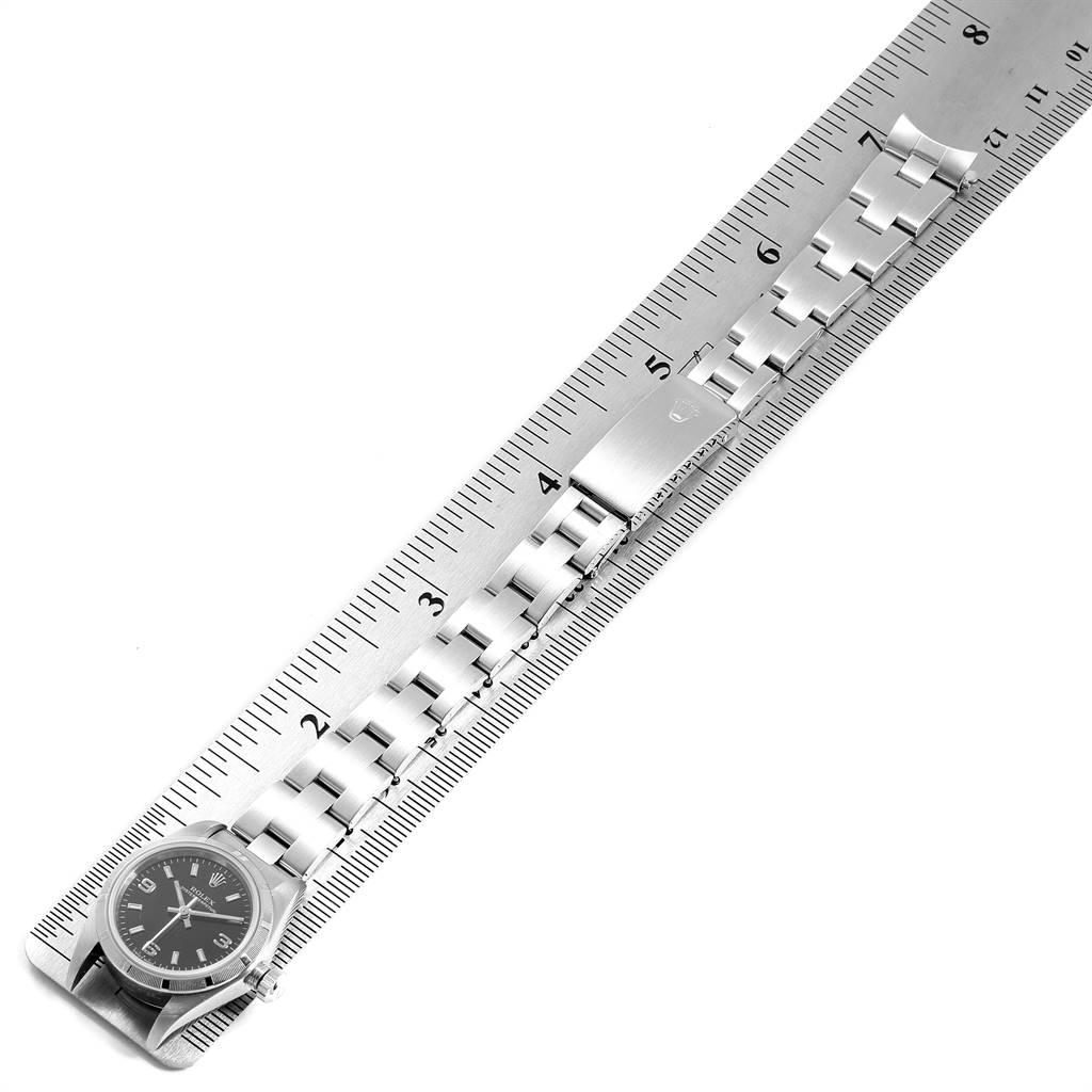 The image shows a Rolex Oyster Perpetual 76030 Women's Stainless Steel Black Dial 76030 Women's Stainless Steel Black Dial watch laid flat on a ruler, displaying the watch face and bracelet.