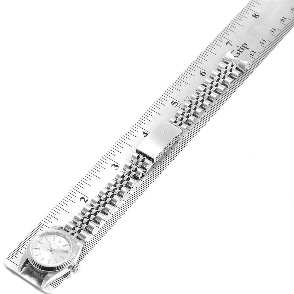 The image shows an overhead view of a Rolex Oyster Perpetual 76094 Women's Stainless Steel Silver Dial 76094 Women's Stainless Steel Silver Dial watch, with its bracelet laid out on a ruler.