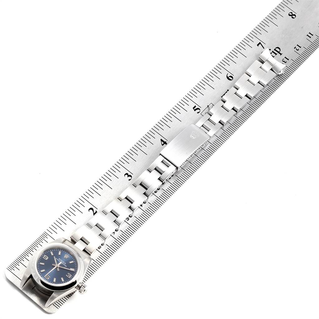 The image shows a top-down view of a Rolex Oyster Perpetual 76080 Women's Stainless Steel Blue Dial 76080 Women's Stainless Steel Blue Dial watch with its bracelet laid out next to a ruler.