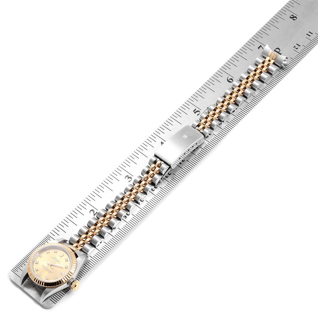 The Rolex Oyster Perpetual 76193 Women
s Steel and Gold (two tone) Champagne Dial 76193 Women
s Steel and Gold (two tone) Champagne Dial watch is shown from an overhead angle, displaying its face, bezel, crown, and bracelet against a ruler.