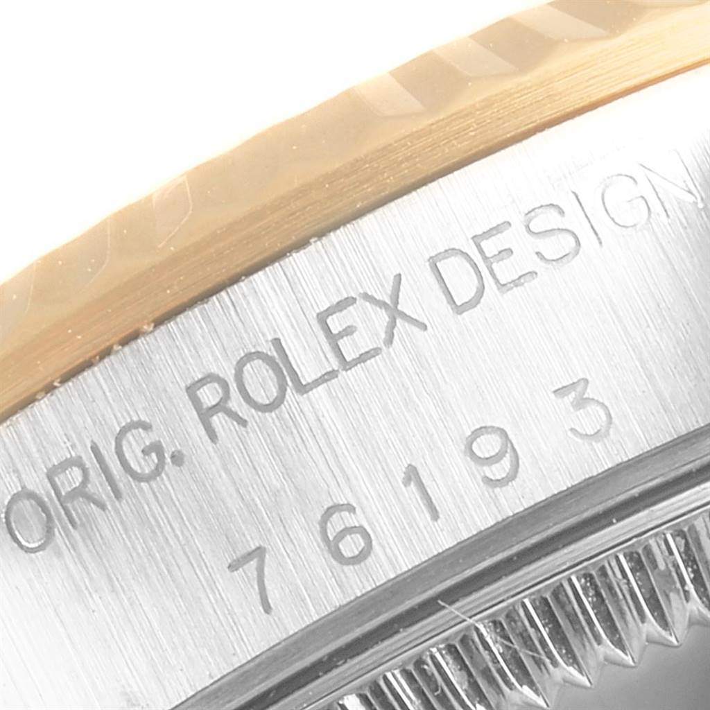 The image shows a close-up of the bezel and case edge of a Rolex Oyster Perpetual 76193 Women
s Steel and Gold (two tone) Champagne Dial 76193 Women
s Steel and Gold (two tone) Champagne Dial watch with a partial view of its serial number.