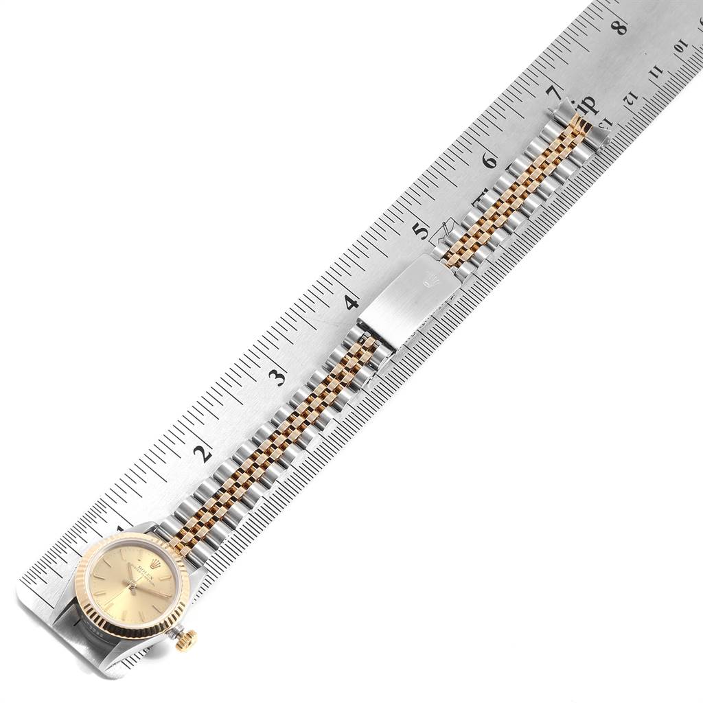 The Rolex Oyster Perpetual 67193 Women
s Steel and Gold (two tone) Champagne Dial 67193 Women
s Steel and Gold (two tone) Champagne Dial watch is shown from a top-down angle, displaying the face, bezel, and bracelet next to a ruler.