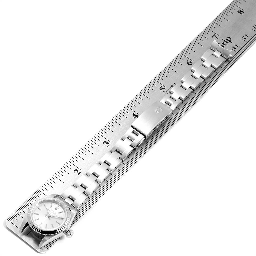 The Rolex Oyster Perpetual 76094 Women's Stainless Steel Silver Dial 76094 Women's Stainless Steel Silver Dial watch is shown from a top-down angle, displaying both its face and bracelet alongside a ruler for measurement.