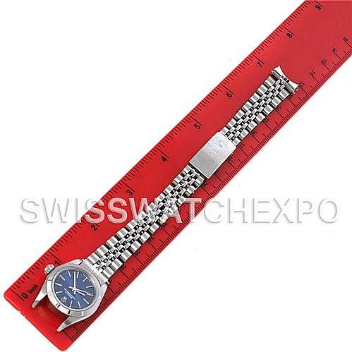 The Rolex Oyster Perpetual 67180 Women's Stainless Steel Blue Dial 67180 Women's Stainless Steel Blue Dial watch is shown from a top-down angle, laid flat on a red ruler with its bracelet fully extended.