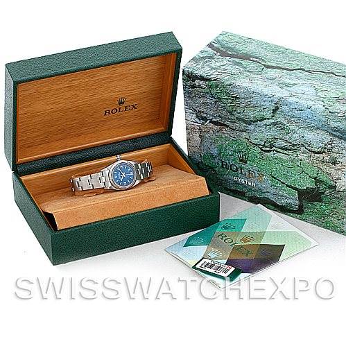 The image shows a Rolex Oyster Perpetual 76030 Women's Stainless Steel Blue Dial 76030 Women's Stainless Steel Blue Dial watch in an open green and wood box, next to its closed box and accompanying documents.