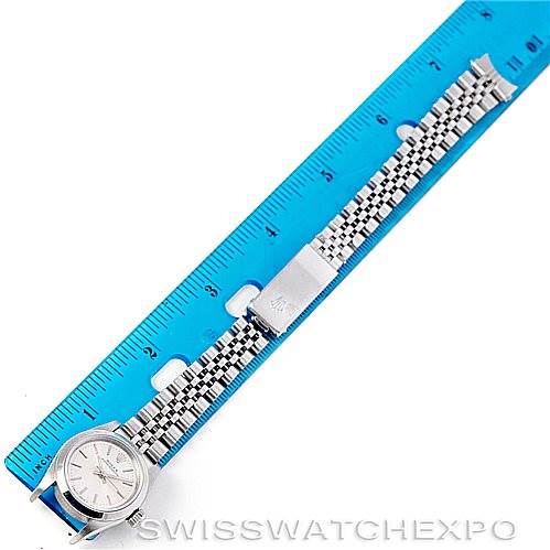The image shows a top-down view of a Rolex Oyster Perpetual 67180 Women's Stainless Steel Silver Dial 67180 Women's Stainless Steel Silver Dial watch placed next to a blue ruler, highlighting the dial and bracelet.
