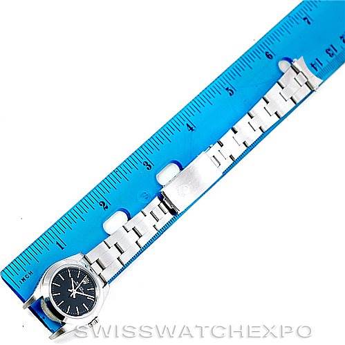 The image shows a Rolex Oyster Perpetual 76080 Women's Stainless Steel Black Dial 76080 Women's Stainless Steel Black Dial watch laid flat next to a ruler, displaying its face, strap, and clasp from a top-down angle.