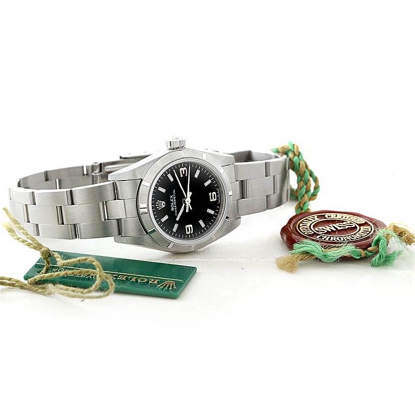 The Rolex Oyster Perpetual 76030 Women's Stainless Steel Black Dial 76030 Women's Stainless Steel Black Dial watch is shown at an angled view, along with its tags and certification seal.