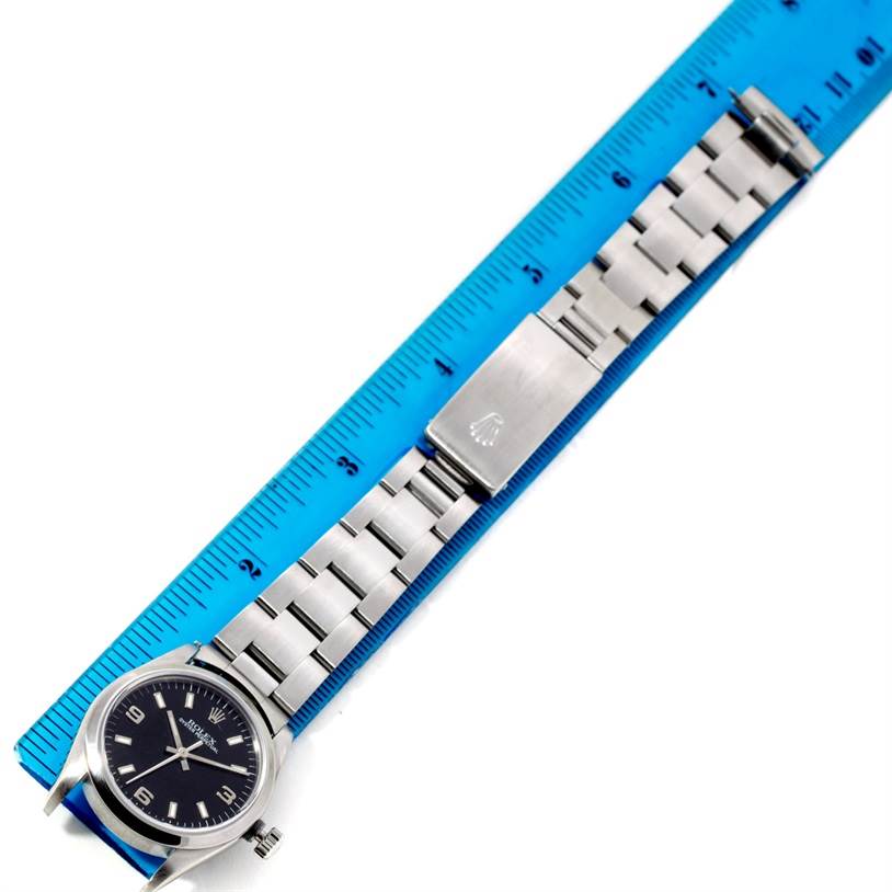 The image shows a top-down view of a Rolex Oyster Perpetual 67180 Women's Stainless Steel Black Dial 67180 Women's Stainless Steel Black Dial watch with its stainless steel bracelet, next to a blue ruler.