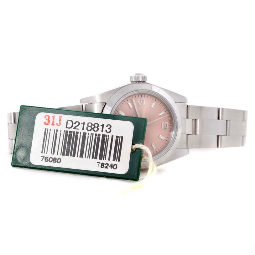 The Rolex Oyster Perpetual 76080 Women's Stainless Steel Pink Dial 76080 Women's Stainless Steel Pink Dial watch is displayed at an angle showing the face, part of the bracelet, and a tag with a barcode.