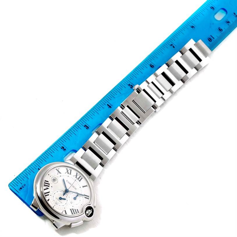 The image shows a Ballon Bleu model watch by Cartier laid next to a blue ruler, displaying both the watch face and metal bracelet.