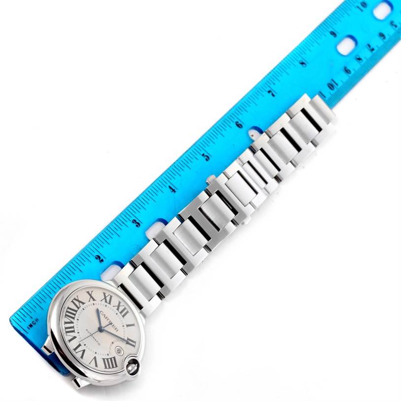 The Ballon Bleu de Cartier watch is shown from a top view next to a blue ruler, highlighting the face and metal bracelet.