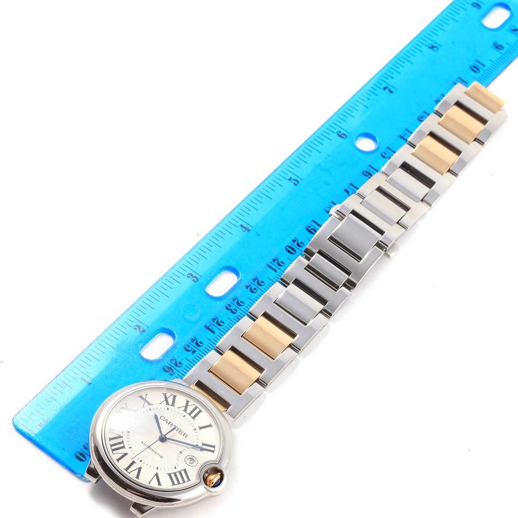 The image shows a Ballon Bleu de Cartier watch placed next to a ruler, highlighting its face and metal strap.