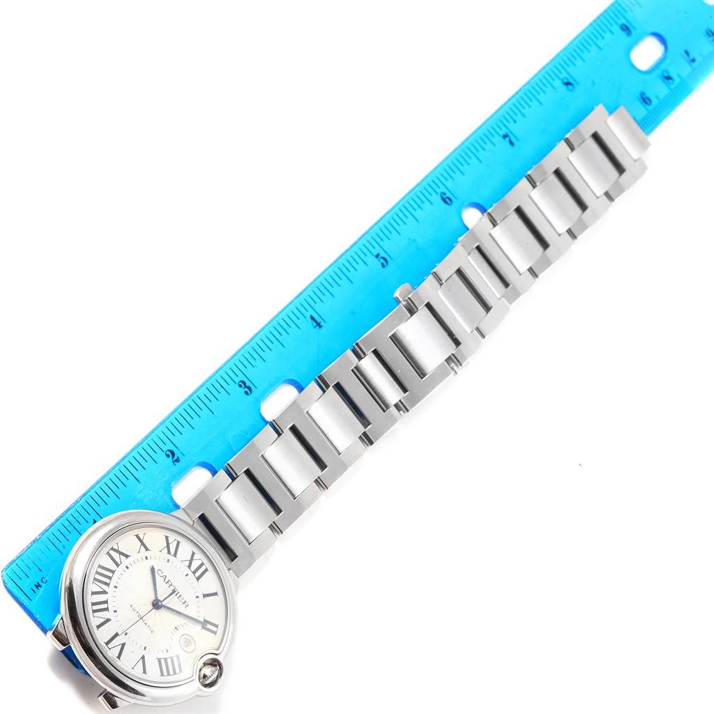 The image shows a Ballon Bleu model by Cartier, focusing on the watch face and metal bracelet, with a blue ruler for scale.