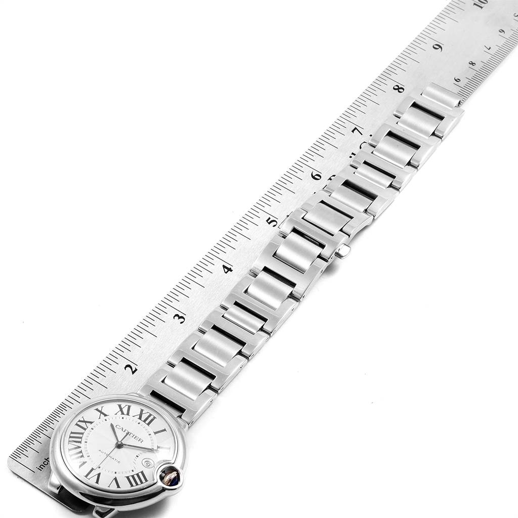 The image shows a Ballon Bleu de Cartier watch lying flat next to a ruler, displaying the face and bracelet.