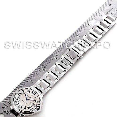 The image shows a Ballon Bleu model by Cartier from a top-down angle, focusing on the watch face and metal bracelet next to a ruler.