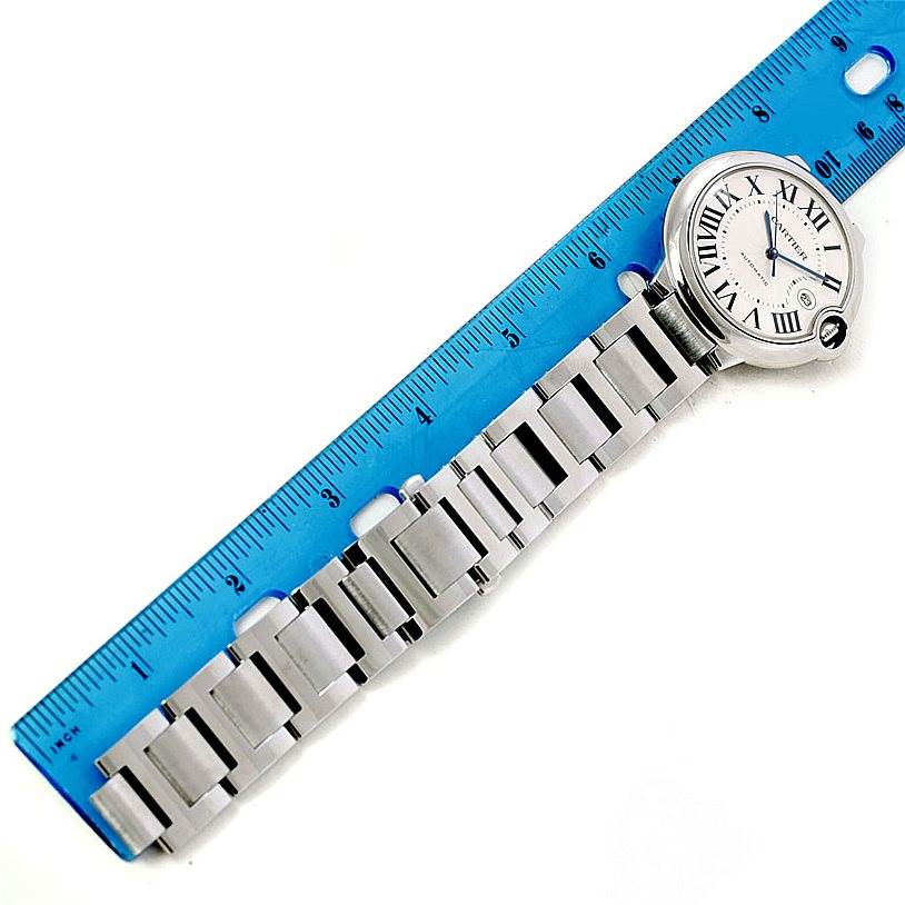 The image shows a Ballon Bleu de Cartier watch laid next to a ruler, showing the case and part of the metal bracelet.