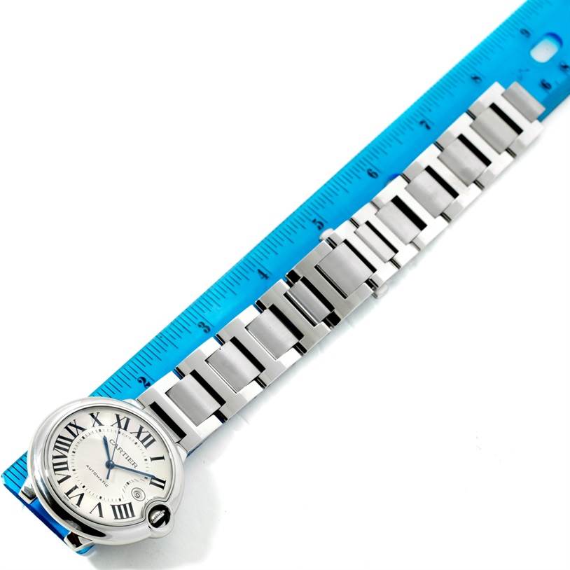 The image shows the Ballon Bleu watch by Cartier from an overhead angle, displaying its face and metal bracelet next to a ruler.