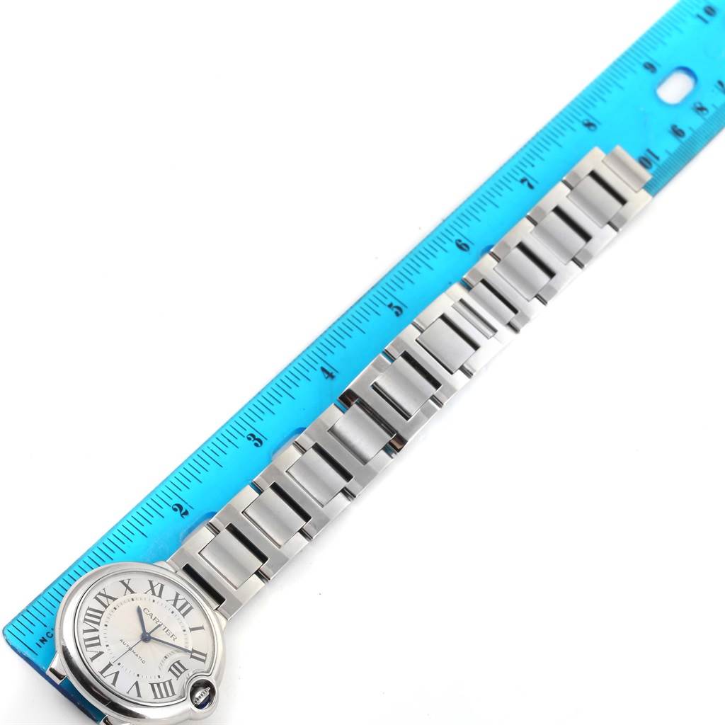 The image shows a Cartier Ballon Bleu W6920046 Men
s Stainless Steel Silver Dial W6920046 Men
s Stainless Steel Silver Dial watch laying flat, face-up, next to a blue ruler.