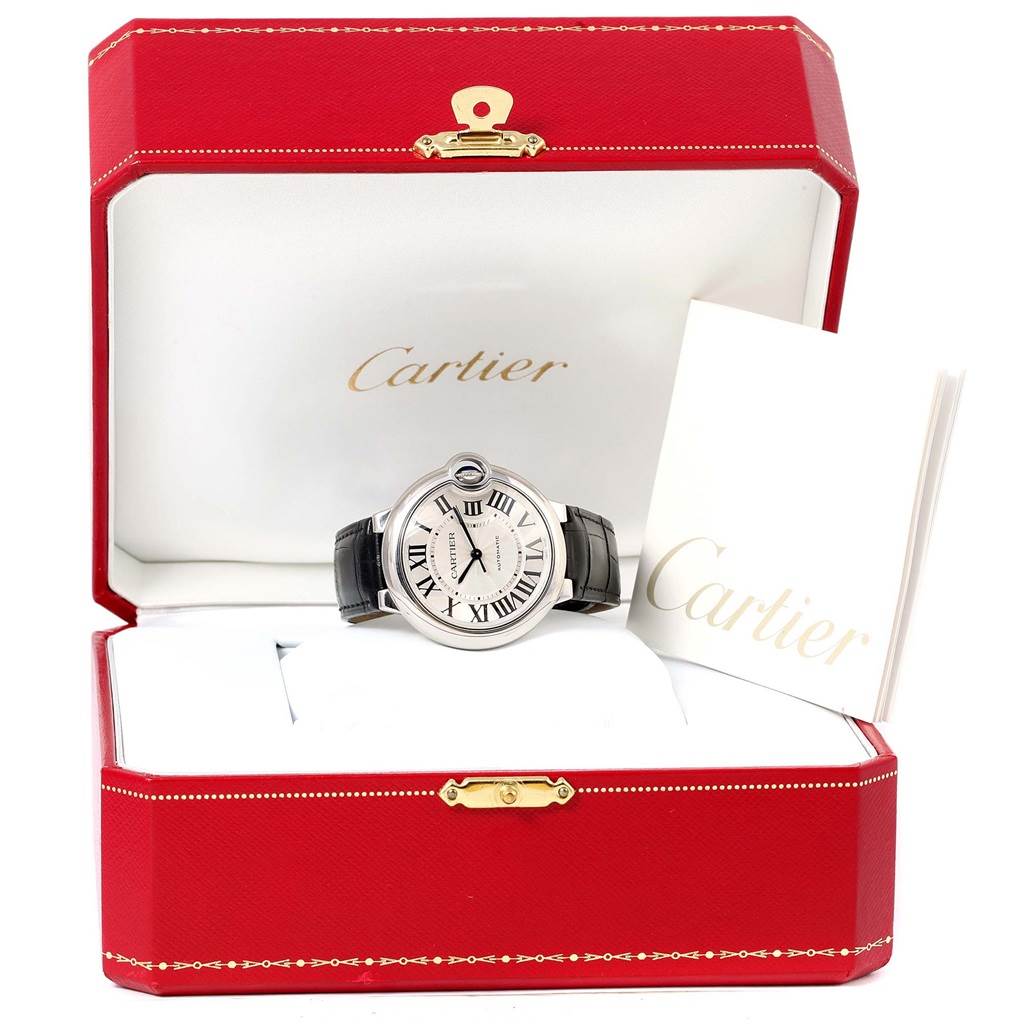 The Ballon Bleu by Cartier watch is shown front-facing in its open red case with a booklet on the right.