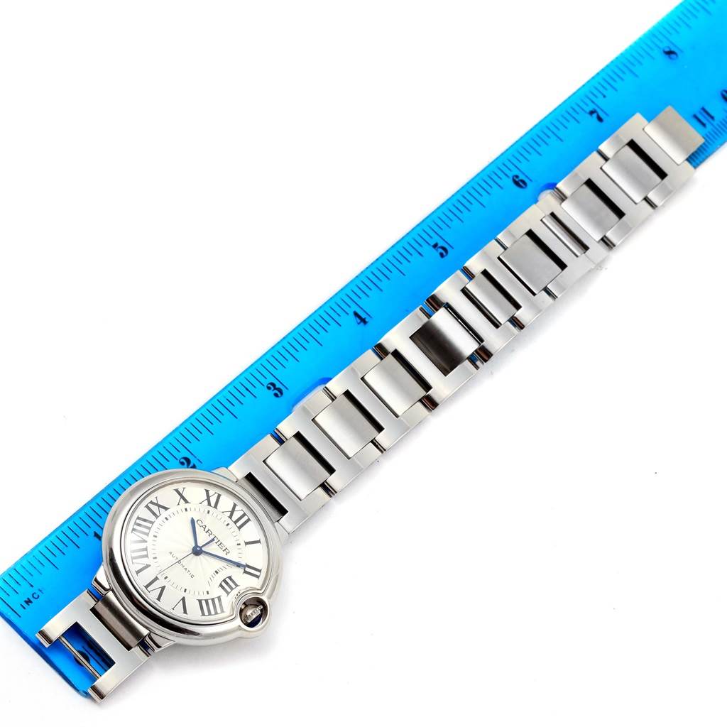 The image shows a Cartier Ballon Bleu W6920046 Women
s Stainless Steel Silver Dial W6920046 Women
s Stainless Steel Silver Dial watch laid flat, next to a blue ruler, displaying the face and metal link bracelet.