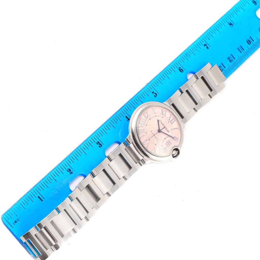This Cartier Ballon Bleu W6920041 Women's Stainless Steel Pink Dial W6920041 Women's Stainless Steel Pink Dial watch is shown lying flat with its bracelet and face visible, next to a blue ruler for scale.