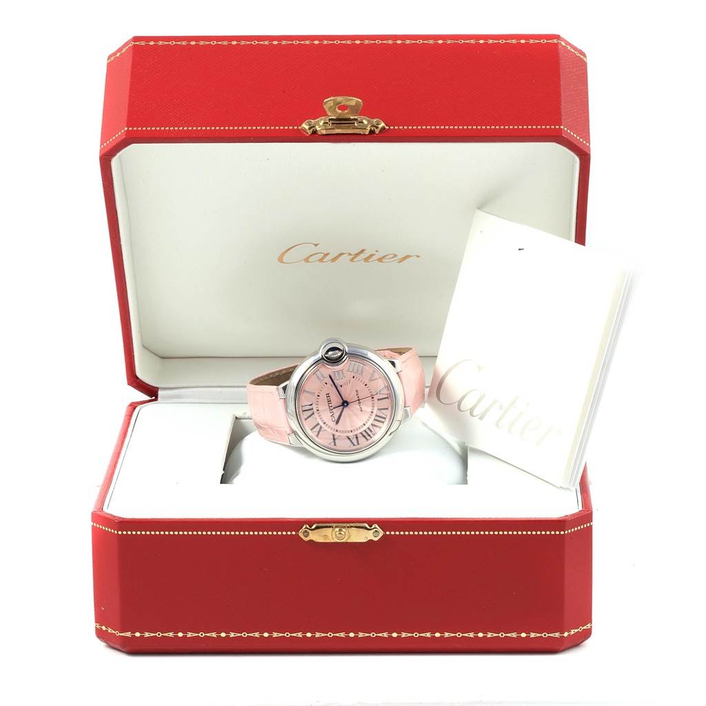 The image shows the Cartier Ballon Bleu WSBB0007 Women
s Stainless Steel Pink Dial WSBB0007 Women
s Stainless Steel Pink Dial watch and its red, open display box with a booklet inside.