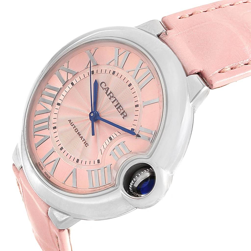 The image shows the Cartier Ballon Bleu WSBB0007 Women
s Stainless Steel Pink Dial WSBB0007 Women
s Stainless Steel Pink Dial watch at a slight angle, highlighting its pink dial, blue hands, Roman numerals, and pink strap.