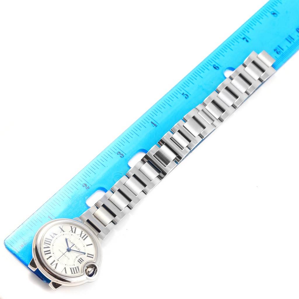 The image shows the Ballon Bleu model by Cartier laid flat with the bracelet and face visible, placed next to a blue ruler for scale.