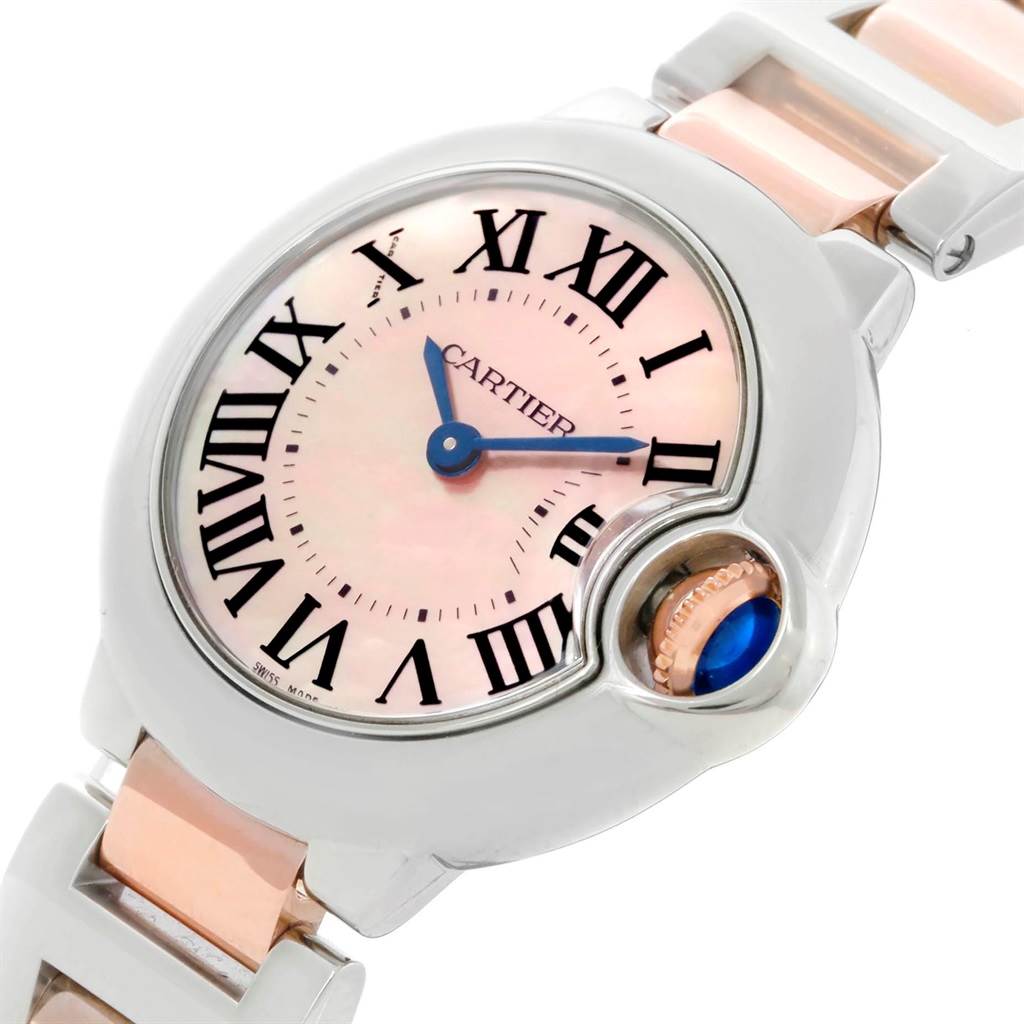 The image shows a close-up of the Cartier Ballon Bleu W6920034 Women's Steel and Gold (two tone) Mother of Pearl Dial W6920034 Women's Steel and Gold (two tone) Mother of Pearl Dial watch, highlighting the face, Roman numerals, blue hands, and crown.