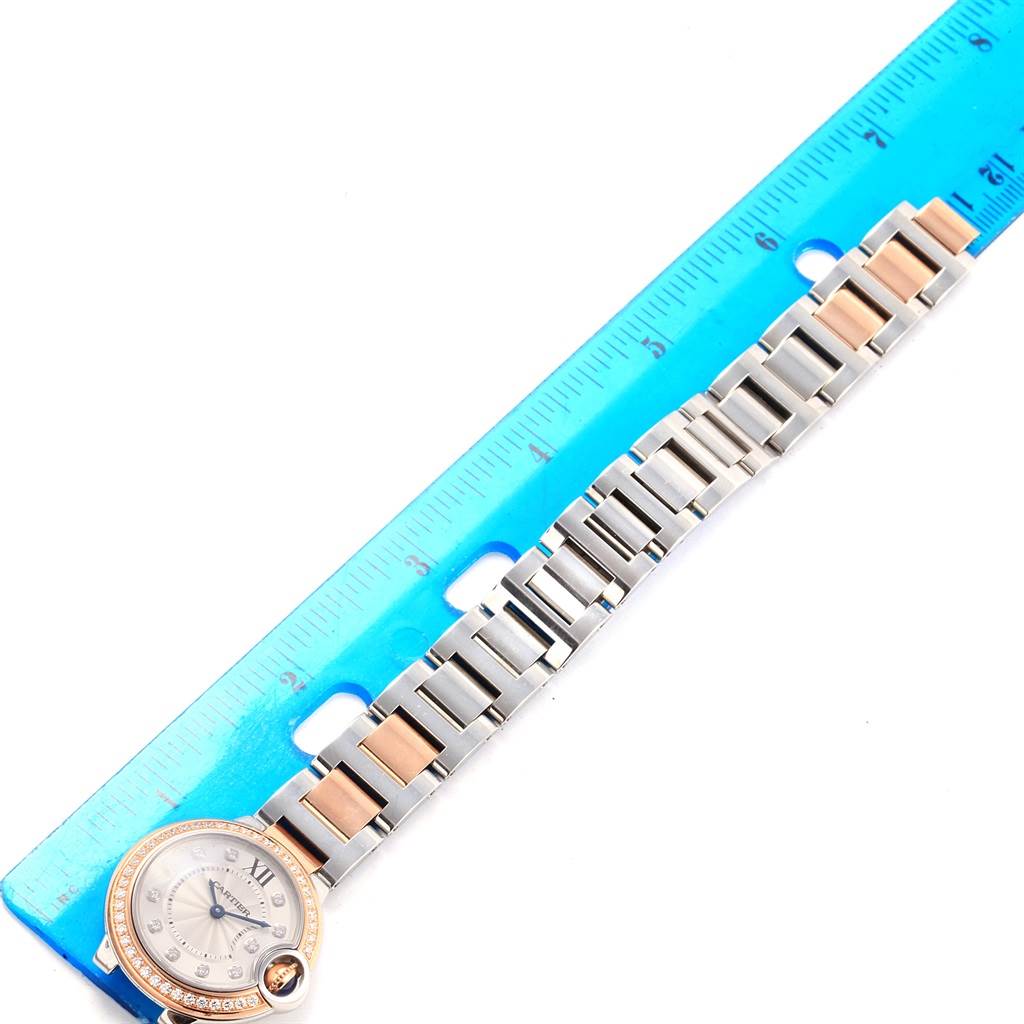 The image shows the Cartier Ballon Bleu WE902076 Women
s Steel and Gold (two tone) Silver Dial WE902076 Women
s Steel and Gold (two tone) Silver Dial watch laid flat, with a focus on its stainless steel and rose gold bracelet measured against a ruler.