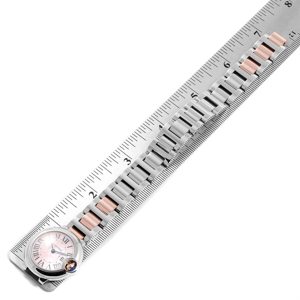 The image shows a Ballon Bleu de Cartier watch placed along a ruler, focusing on the entire band and face from an angled top-down view.