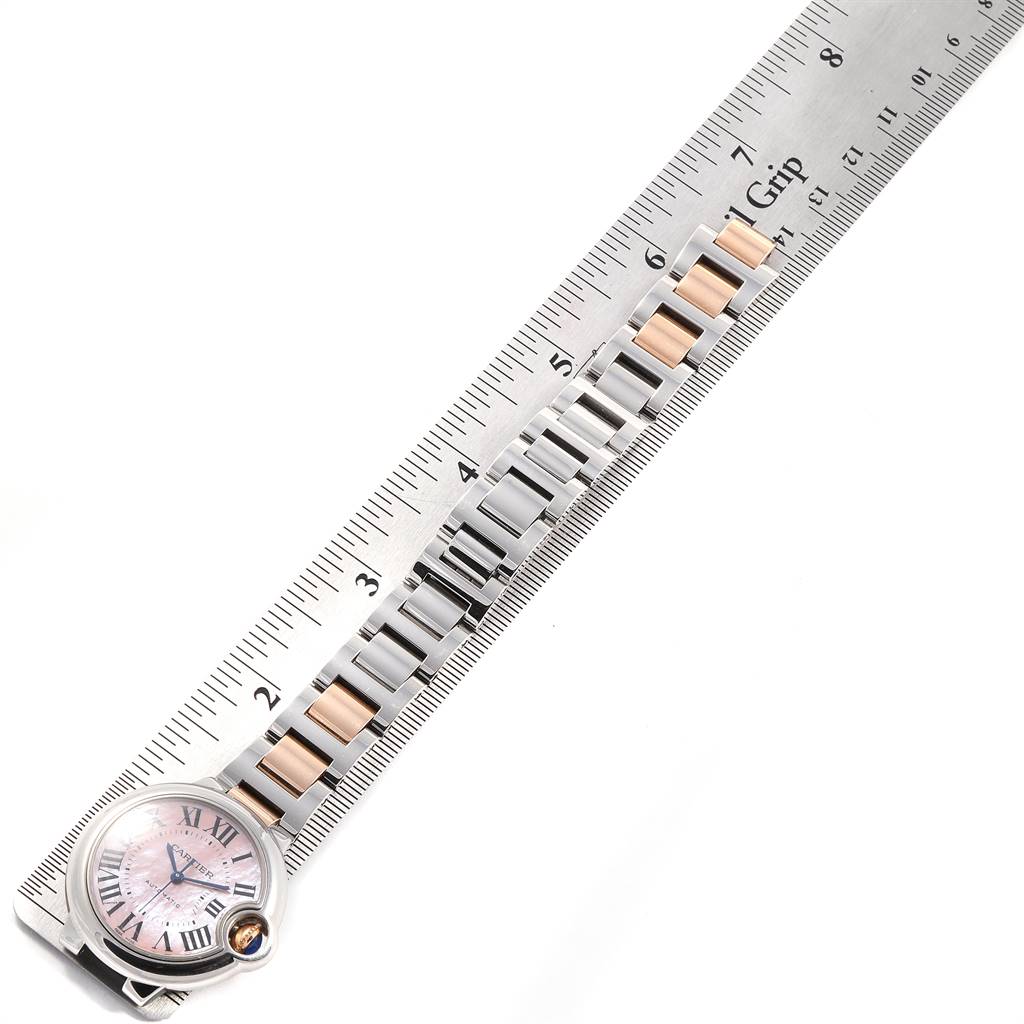 The image shows the watch face and part of the metal band of a Cartier Ballon Bleu W6920098 Women
s Steel and Gold (two tone) Mother of Pearl Dial W6920098 Women
s Steel and Gold (two tone) Mother of Pearl Dial model, positioned alongside a ruler.