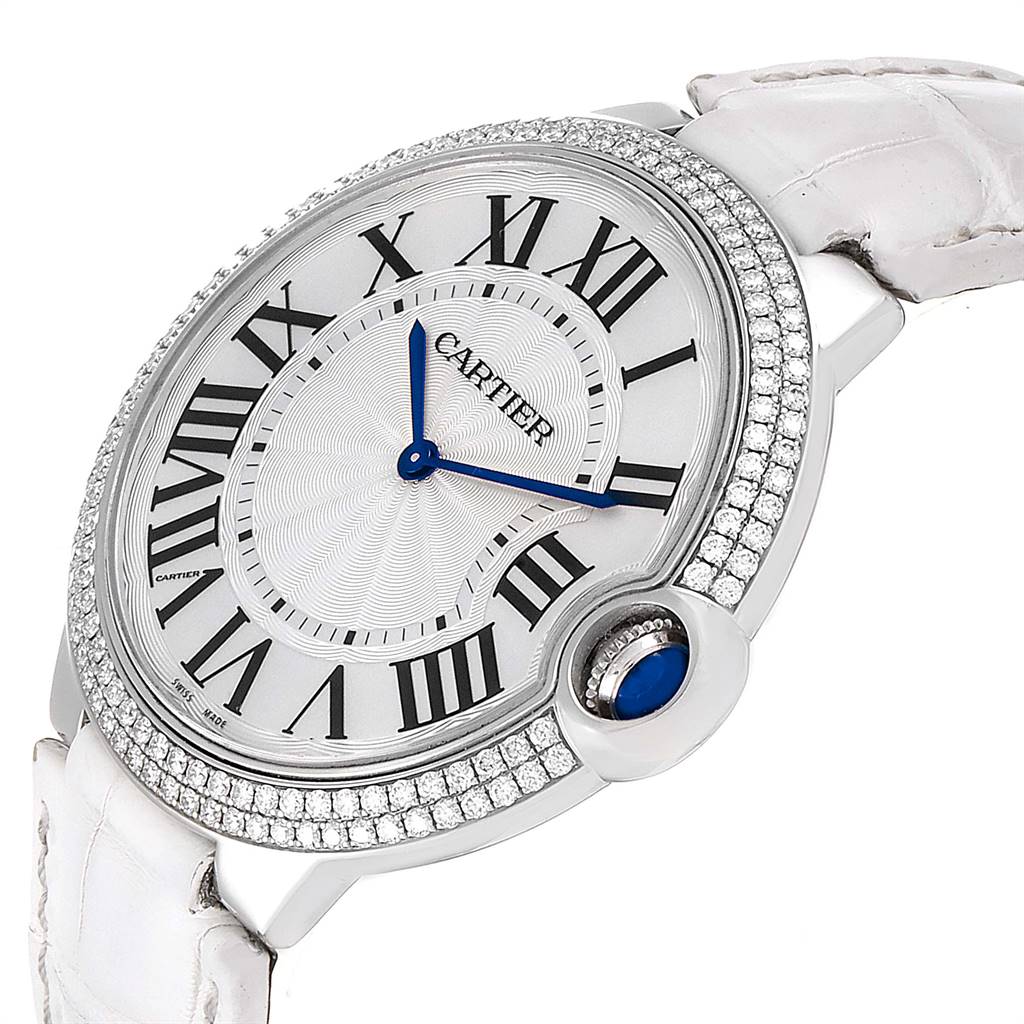 The image shows a close-up, angled view of the Cartier Ballon Bleu WE902056 Women's White Gold Silver Dial WE902056 Women's White Gold Silver Dial watch face and part of the strap, highlighting the Roman numerals and blue sapphire cabochon crown.