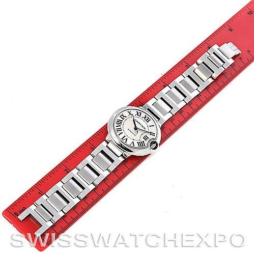 This image shows an overhead view of a Cartier Ballon Bleu W6920046 Stainless Steel Silver Dial W6920046 Stainless Steel Silver Dial watch placed on a red ruler, displaying the face and bracelet fully.