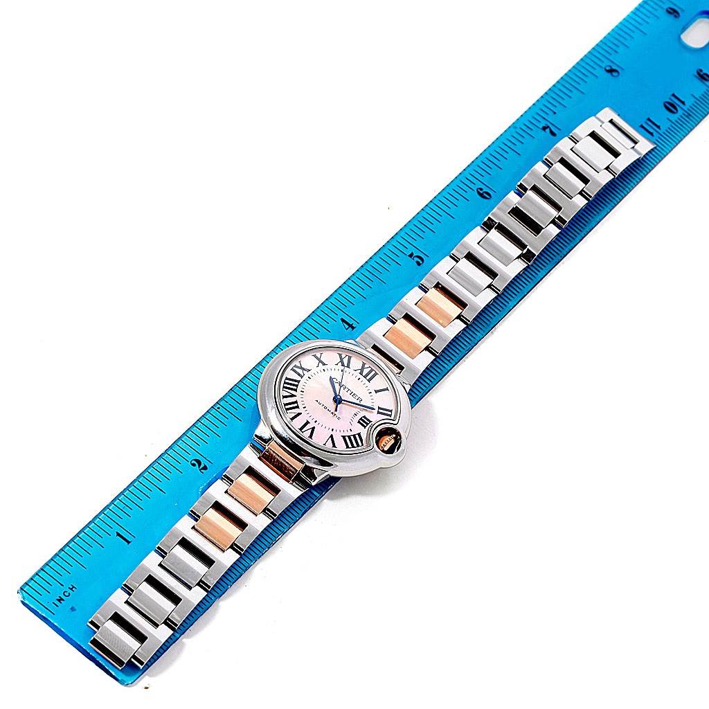 The Ballon Bleu model by Cartier is shown from a top-down angle, showcasing its face, blue hands, Roman numerals, and bracelet with a ruler for scale.