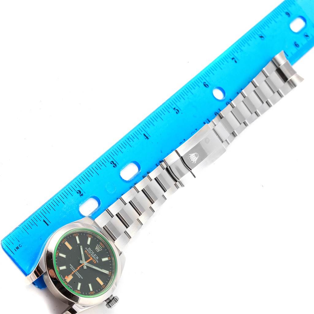The image shows the Rolex Milgauss 116400V Men's Stainless Steel Black Dial 116400V Men's Stainless Steel Black Dial watch laid flat with its face, bracelet, and clasp visible, alongside a blue ruler.