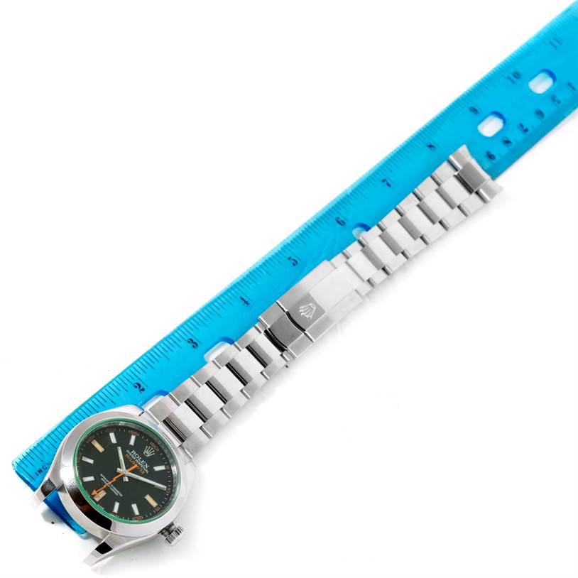 The Rolex Milgauss 116400V Men's Stainless Steel Black Dial 116400V Men's Stainless Steel Black Dial watch is shown flat with the face up and positioned next to a blue ruler for measurement.