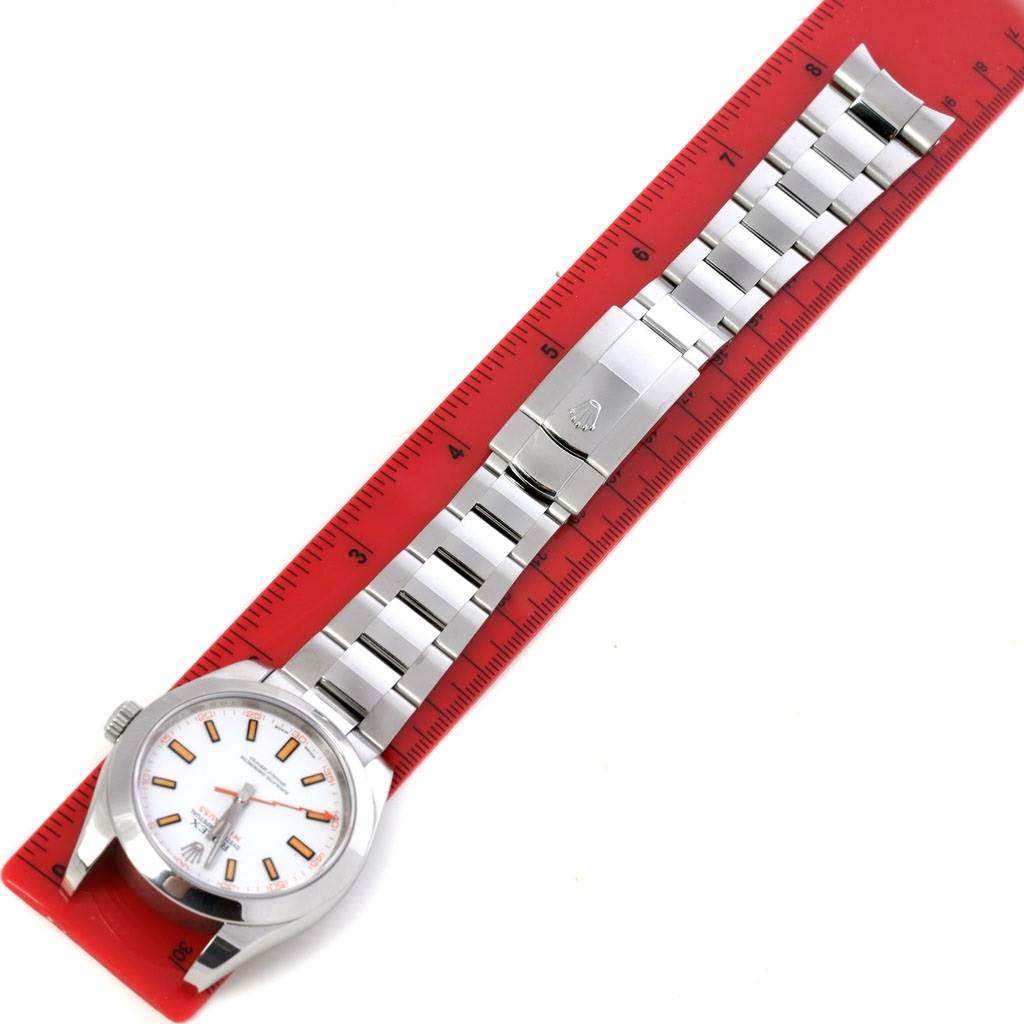 The Rolex Milgauss 116400WSO Men's Stainless Steel White Dial 116400WSO Men's Stainless Steel White Dial watch is shown flat with its full bracelet extended alongside a red ruler for measurement.