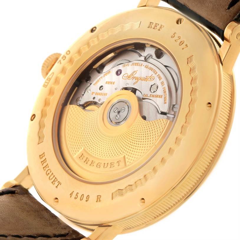 The image shows the back view of a Breguet Classique 5207BA/12/9V6 Men's Yellow Gold Silver Dial 5207BA/12/9V6 Men's Yellow Gold Silver Dial watch, revealing its intricate mechanical movement and engraved details.