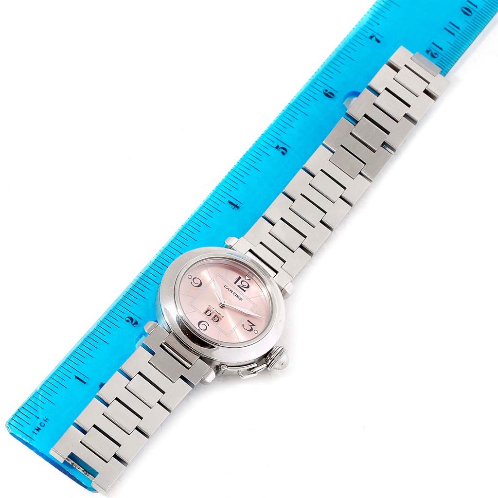 The Cartier Pasha W31058M7 Women's Stainless Steel Pink Dial W31058M7 Women's Stainless Steel Pink Dial watch is shown from a top-down angle, with its face, bracelet, and a ruler for scale.