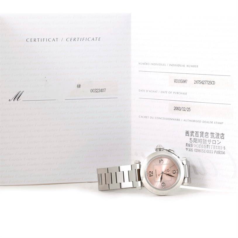 The photo shows the Cartier Pasha W31058M7 Women
s Stainless Steel Pink Dial W31058M7 Women
s Stainless Steel Pink Dial watch placed in front of its certificate, highlighting its face and part of the bracelet.