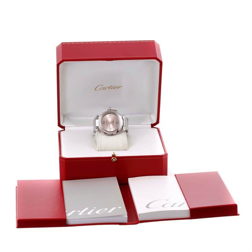 The Cartier Pasha W31058M7 Women
s Stainless Steel Pink Dial W31058M7 Women
s Stainless Steel Pink Dial watch is displayed front-on, inside its open red box, with accompanying booklets laid out in front.